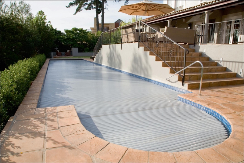 Powerplastic Pools Covers (021 703 5880).This magnificent house in Somerset West was given the fabulous finishing touch by the installation of the Starline Roldeck automatic pool cover. Supplied and installe by PowerPlastics Pool Covers, the cover adds elegance, style and state of the art ease of living. The Roldeck is operated via an on/off switch or a handheld remote. This image features the cover completely closed, preventing dirt from entering the water as well as reducing evaporation and giving the pool area a sophisticated look.